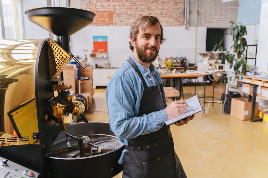 A roaster in an apron checking a coffee roasting machine